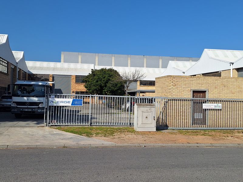 Front exterior view of a commercial industrial property featuring face brick construction, corrugated roofing, and a secure gated entrance with concrete driveway access.