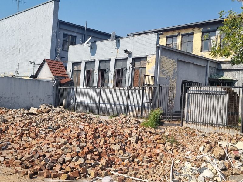 Rear exterior view of the building showing significant construction debris and rubble on the site with metal security fencing.