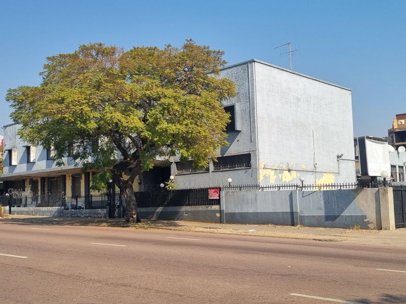Street-facing view of a multi-story commercial or apartment building featuring a masonry boundary wall and perimeter security fencing.