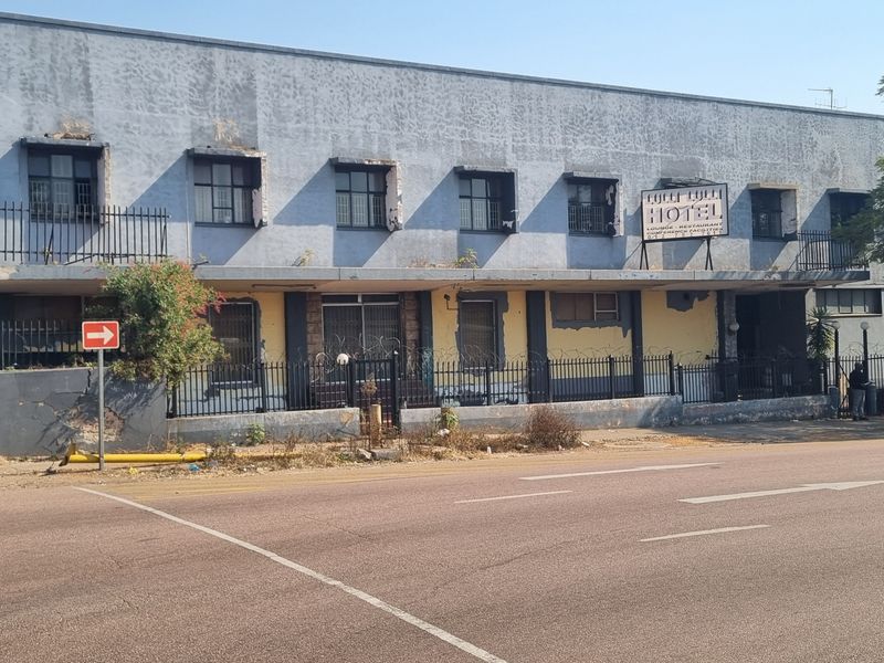 Street-level view of a multi-story commercial building facade featuring security fencing, metal security bars, and a weathered exterior finish.