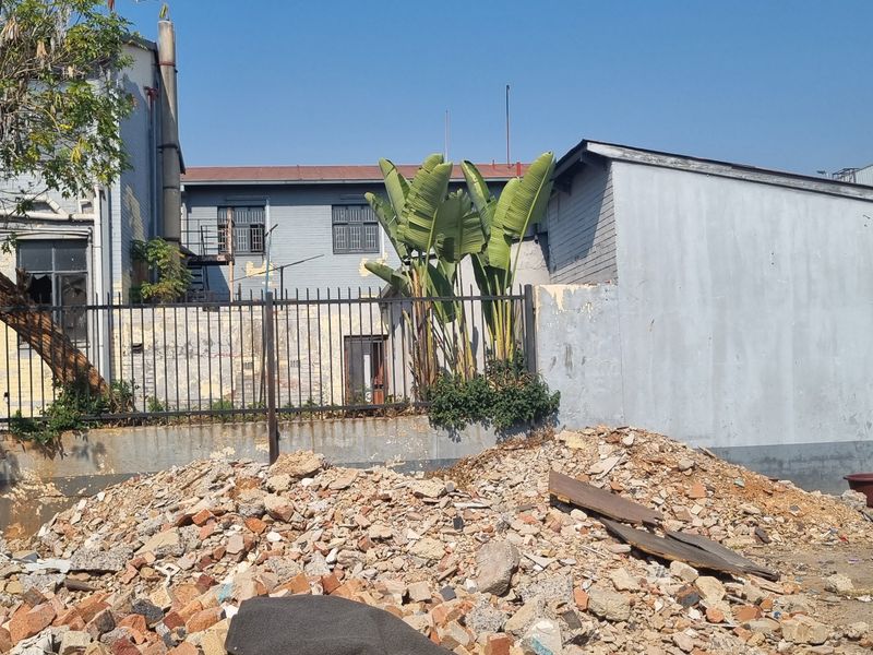 Rear exterior view of the property showing a masonry boundary wall, metal fencing, and significant accumulation of construction debris and rubble on the site.