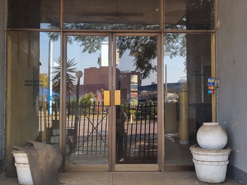 Entrance area featuring glass double doors with metal framing, showing signs of exterior wall paint deterioration and plaster damage.