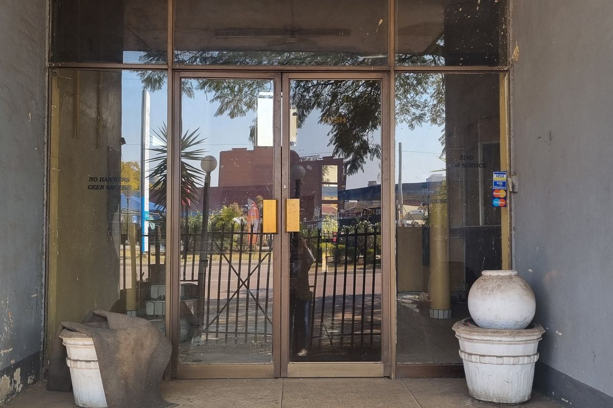 Entrance area featuring glass double doors with metal framing, showing signs of exterior wall paint deterioration and plaster damage.