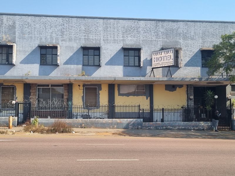 Street-facing view of a commercial building facade featuring a concrete structure, security fencing, and significant exterior paint deterioration.