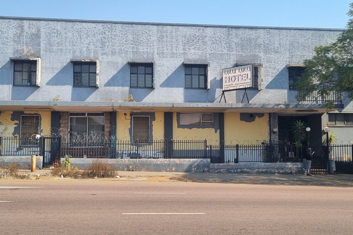 Street-facing view of a commercial building facade featuring a concrete structure, security fencing, and significant exterior paint deterioration.