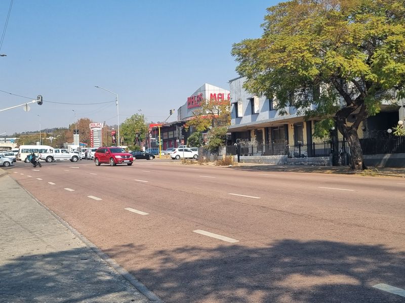 A street-level view showing the surrounding urban infrastructure, including paved sidewalks, road access, and nearby commercial building facades.