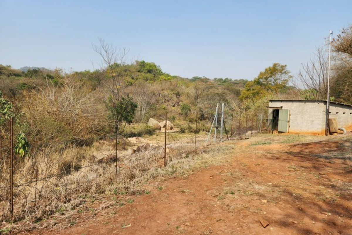 A view of the rear farm grounds featuring a small outbuilding, wire fencing, and natural landscape.