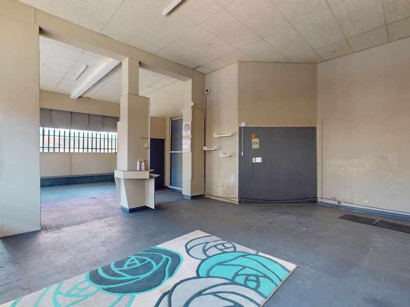 An open-plan commercial space featuring a suspended ceiling, security gate, and built-in counter, currently vacant and requiring cosmetic updates to the flooring and walls.