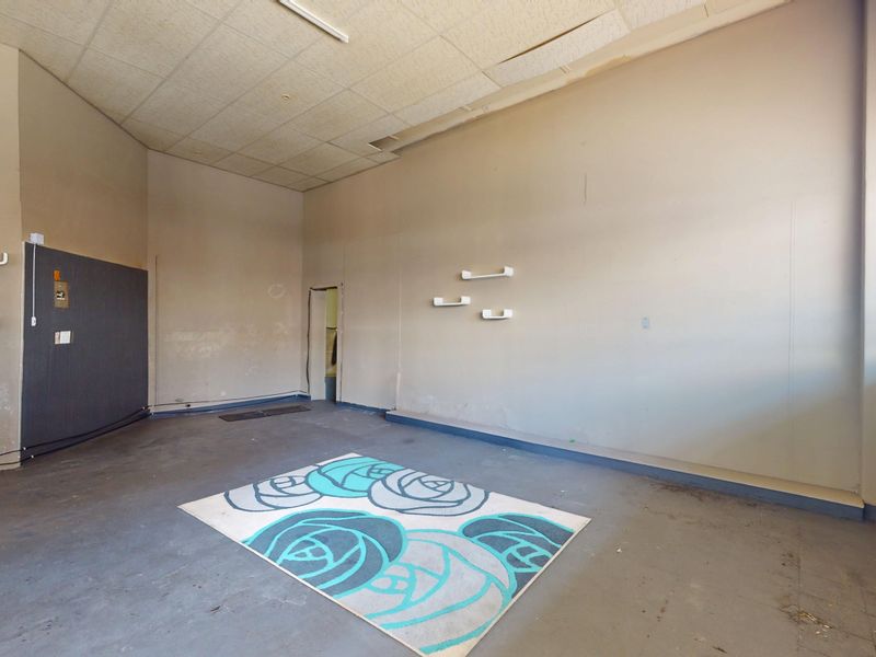 An empty commercial open-plan space featuring concrete flooring, suspended ceiling tiles, and wall-mounted shelving units, requiring cosmetic refurbishment.