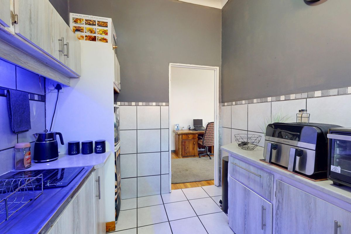 Compact kitchen featuring built-in cabinetry, tiled backsplash, and integrated cooking appliances, with a doorway leading to an adjacent office space.