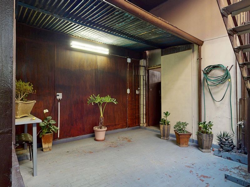 A covered outdoor patio area featuring a metal staircase, corrugated roofing, and paved flooring, showing signs of wear and requiring maintenance.