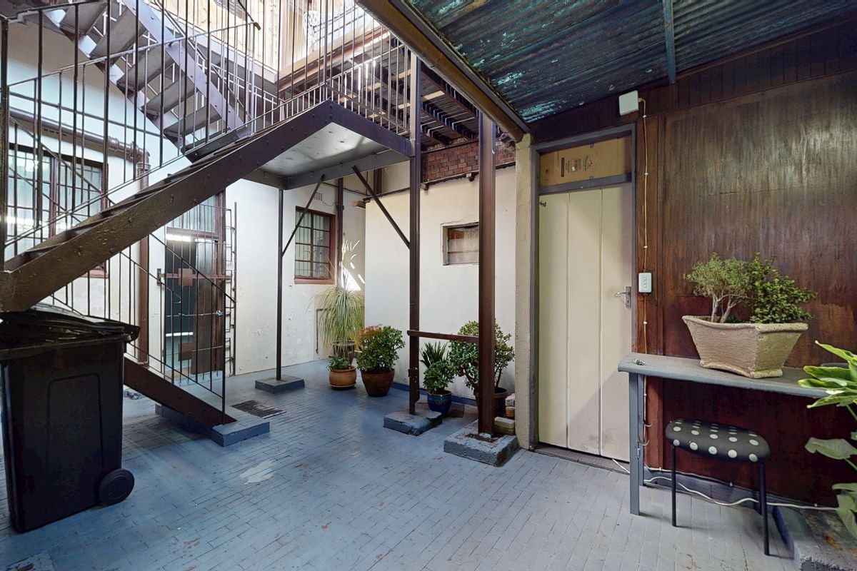 A rear exterior courtyard area featuring a metal staircase, brick paving, and weathered timber wall cladding, providing access to the building's upper levels.