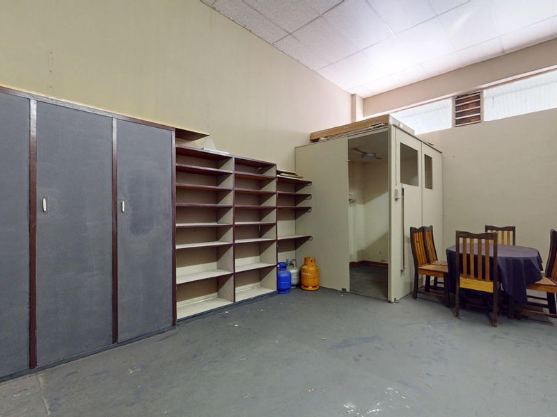 A functional utility or storage space featuring built-in cabinetry, open shelving, and a partitioned office enclosure with a suspended ceiling.