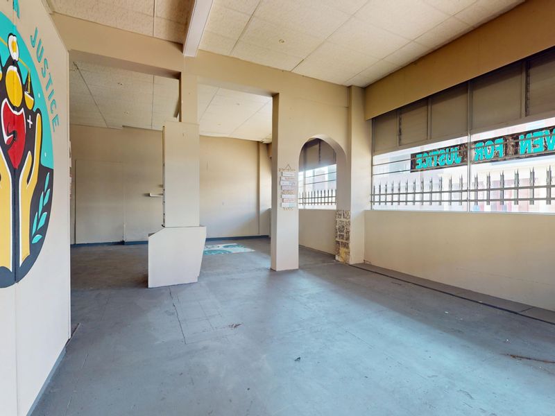 An open-plan commercial space featuring concrete flooring, a suspended ceiling, and security bars on the windows, suitable for various business applications.