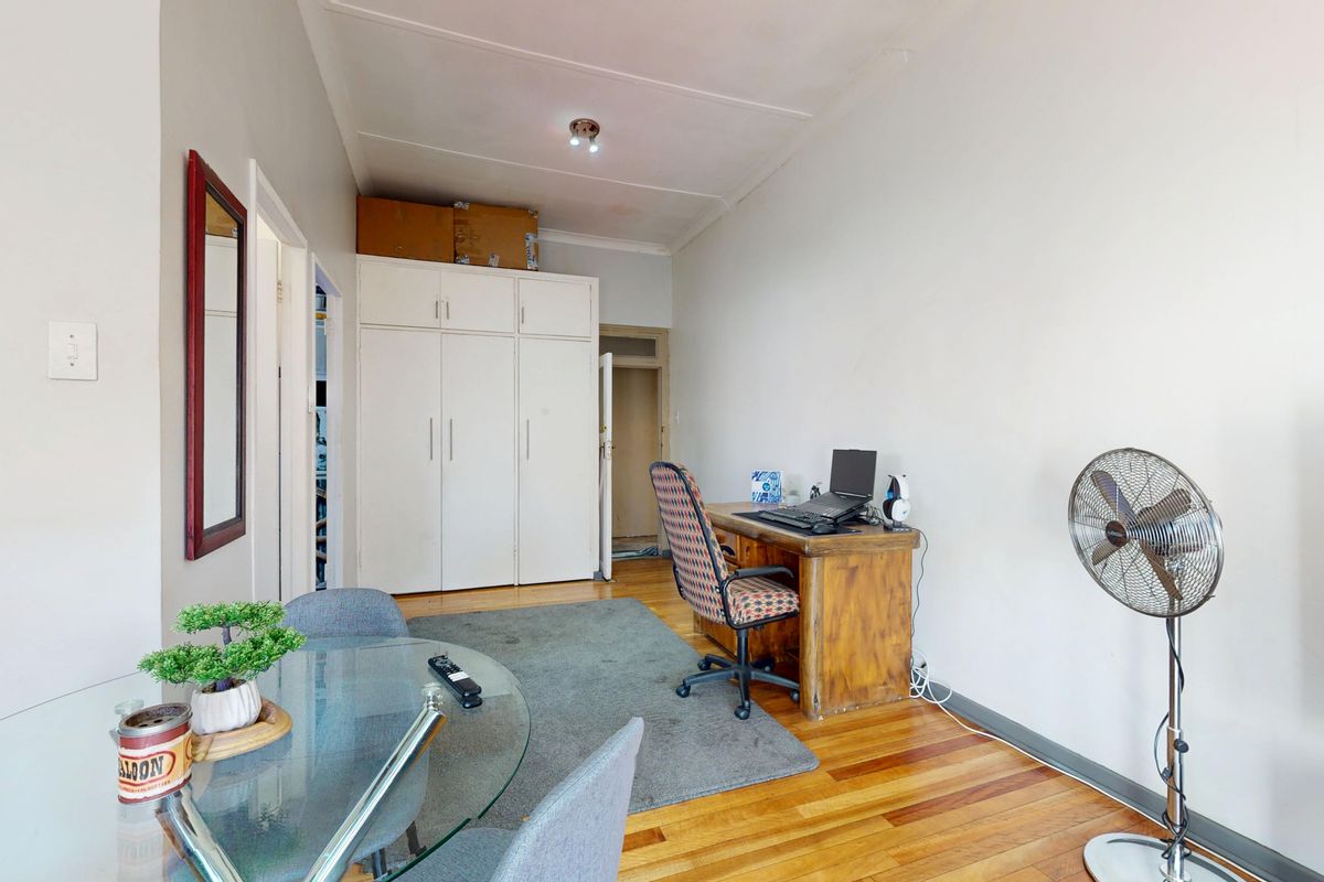 A functional living area featuring hardwood flooring and built-in storage cupboards, offering a versatile space for office or lounge use.