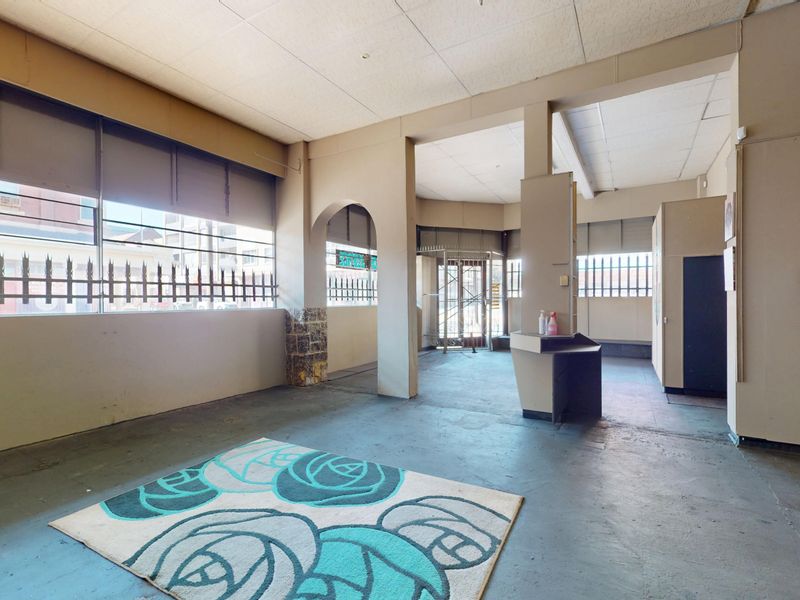 Open-plan commercial space featuring a suspended ceiling, security bars on windows, and a built-in service counter, suitable for various business applications.