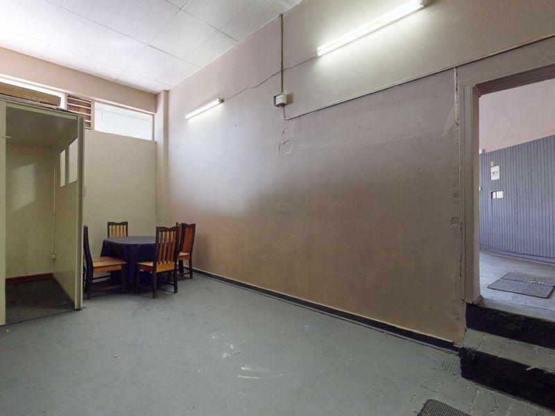 Open plan commercial space featuring a partitioned area, fluorescent lighting, and a small integrated sink unit, requiring cosmetic updates to improve the interior finish.