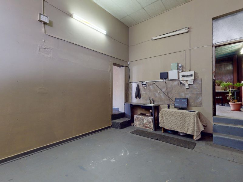 A functional utility space featuring a sink, tiled splashback, and exposed electrical infrastructure, suitable for storage or back-of-house operations.