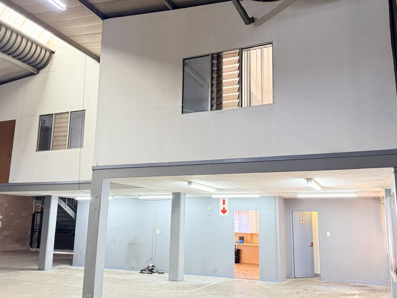 Industrial utility space featuring a mezzanine level, exposed steel roof structure, concrete block walls, and functional fluorescent lighting throughout the open floor area.