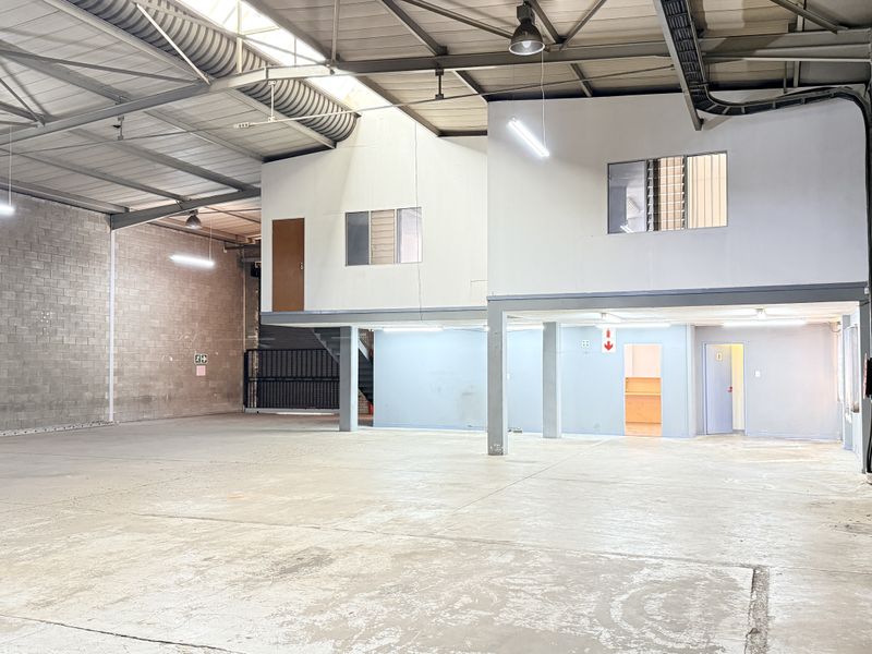 Spacious industrial warehouse unit featuring high ceilings with exposed steel trusses, concrete flooring, and a functional mezzanine level for additional office or storage space.