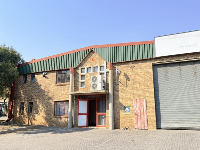 Front elevation of an industrial property featuring face brick construction, a large roller shutter door, and paved driveway access.
