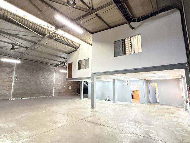 Spacious industrial warehouse unit featuring high ceilings with exposed steel trusses, concrete flooring, and a functional mezzanine level with internal office space.