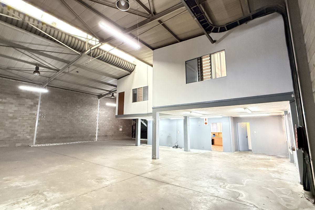 Spacious industrial warehouse unit featuring high ceilings with exposed steel trusses, concrete flooring, and a functional mezzanine level with internal office space.