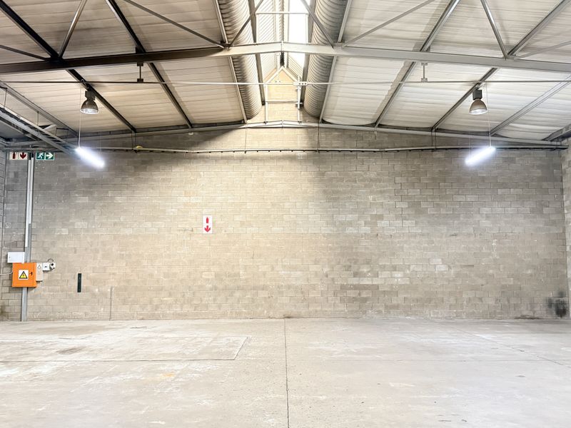 Spacious industrial warehouse unit featuring high ceilings with exposed steel trusses, concrete block walls, and durable concrete flooring, suitable for various commercial operations.