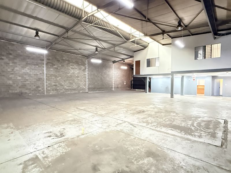 Spacious industrial warehouse unit featuring high ceilings with exposed steel trusses, concrete flooring, and a mezzanine level for additional office or storage space.