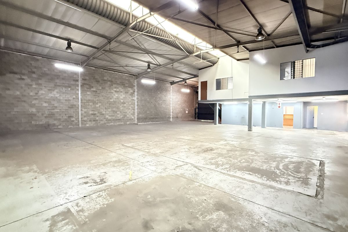 Spacious industrial warehouse unit featuring high ceilings with exposed steel trusses, concrete flooring, and a mezzanine level for additional office or storage space.