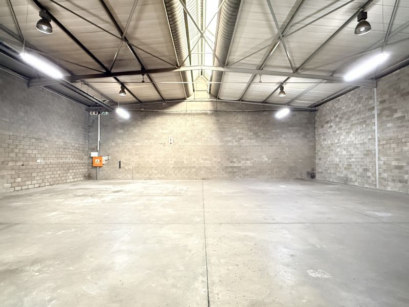 Spacious industrial warehouse unit featuring high ceilings with exposed steel trusses, durable concrete block walls, and polished concrete flooring.