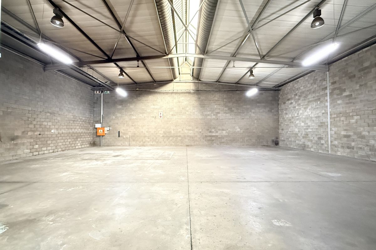 Spacious industrial warehouse unit featuring high ceilings with exposed steel trusses, durable concrete block walls, and polished concrete flooring.