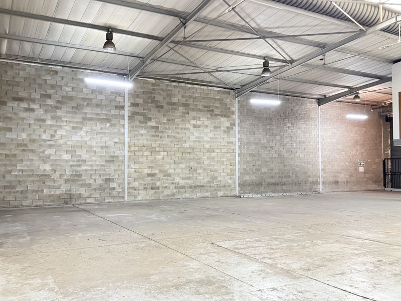 Spacious industrial warehouse unit featuring high ceilings with exposed steel trusses, durable concrete block walls, polished concrete flooring, and a mezzanine level.