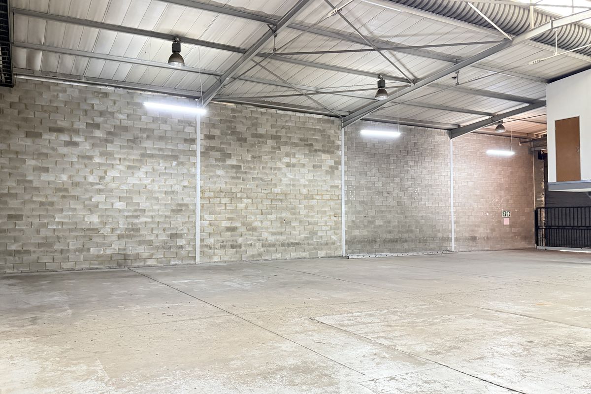 Spacious industrial warehouse unit featuring high ceilings with exposed steel trusses, durable concrete block walls, polished concrete flooring, and a mezzanine level.