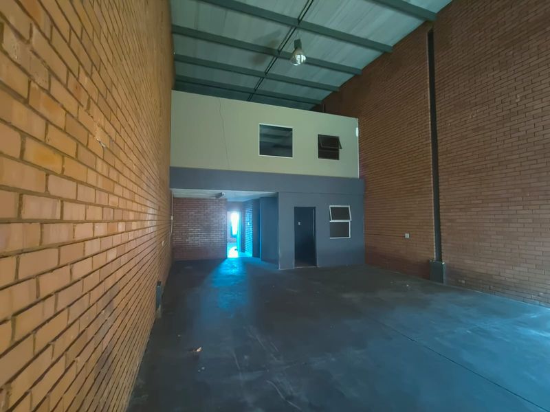Spacious industrial utility area featuring exposed brick walls, concrete flooring, and a mezzanine level, suitable for storage or workshop use.
