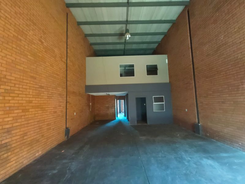 Spacious industrial warehouse unit featuring high ceilings with exposed steel trusses, raw brick walls, concrete flooring, and a functional mezzanine level.