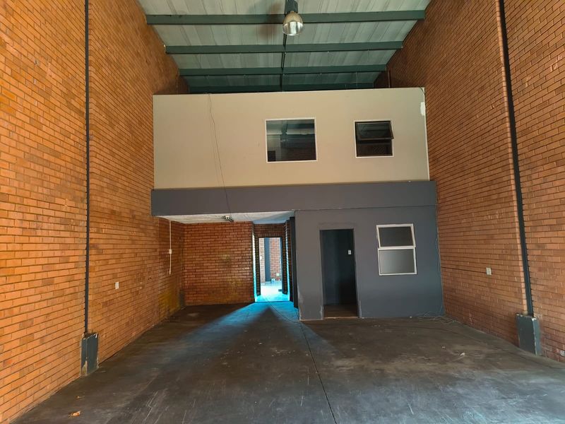 Spacious industrial utility area featuring exposed brick walls, concrete flooring, and a mezzanine level, suitable for workshop, storage, or light industrial operations.