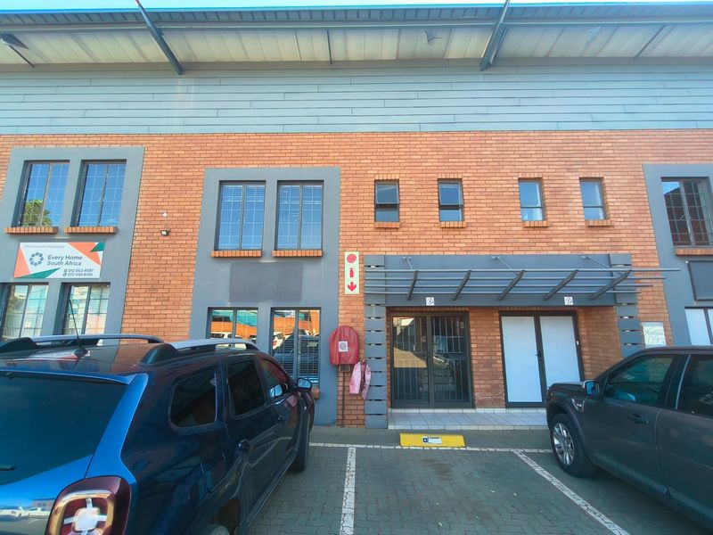 Front elevation of an industrial brick building featuring a metal roof, security gate entrance, and dedicated paved parking bays.