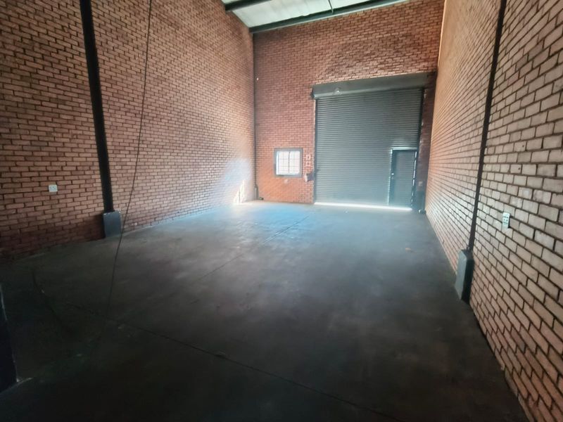 Spacious industrial warehouse unit featuring high exposed brick walls, concrete flooring, and a large roller shutter door for easy access.