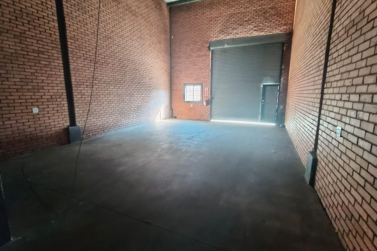 Spacious industrial warehouse unit featuring high exposed brick walls, concrete flooring, and a large roller shutter door for easy access.