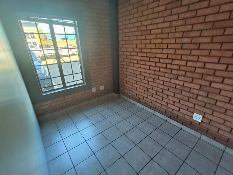 A clean, empty office space featuring exposed brick walls, tiled flooring, and a window with security bars, suitable for a professional workspace.