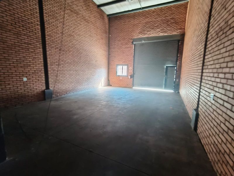 Spacious industrial utility unit featuring high exposed brick walls, concrete flooring, and a large roller shutter door for easy access.