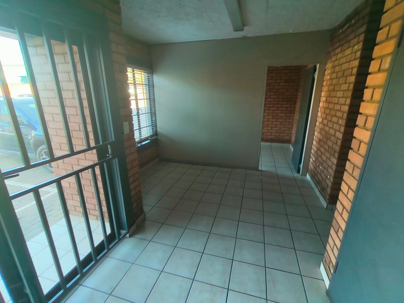 An empty entrance area featuring exposed brick walls, tiled flooring, and a secure metal gate, providing a functional industrial-style access point.