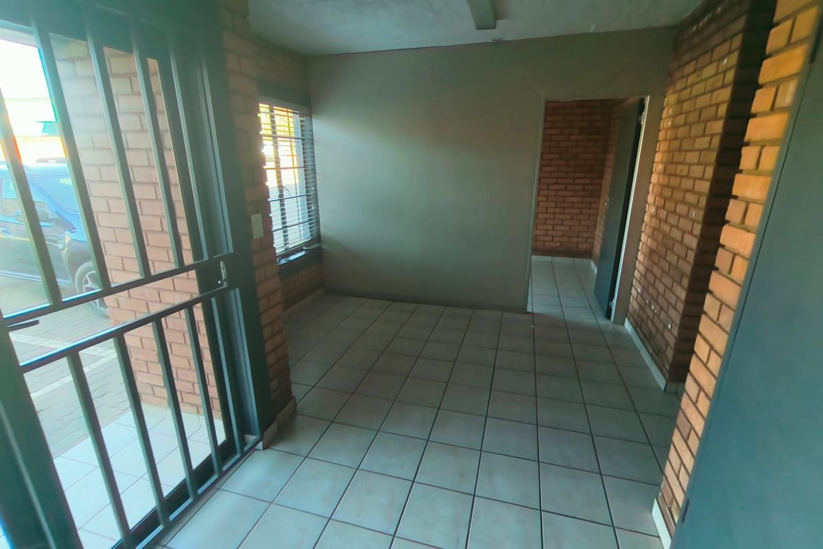An empty entrance area featuring exposed brick walls, tiled flooring, and a secure metal gate, providing a functional industrial-style access point.