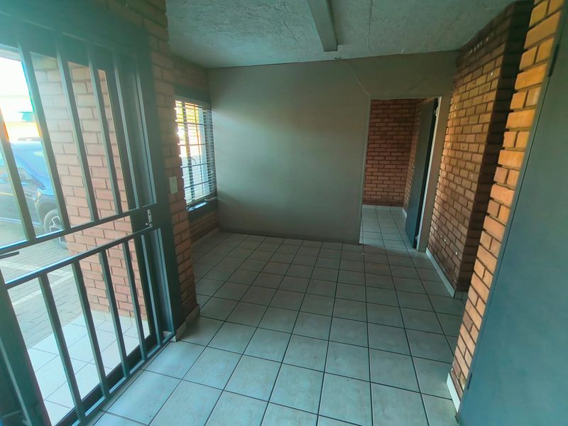 An empty industrial-style entry area featuring exposed brick walls, tiled flooring, and a secure metal entrance gate.