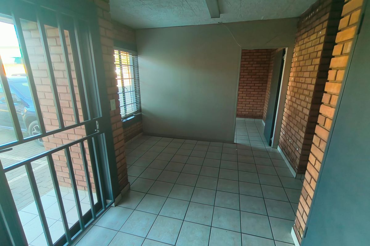 An empty industrial-style entry area featuring exposed brick walls, tiled flooring, and a secure metal entrance gate.