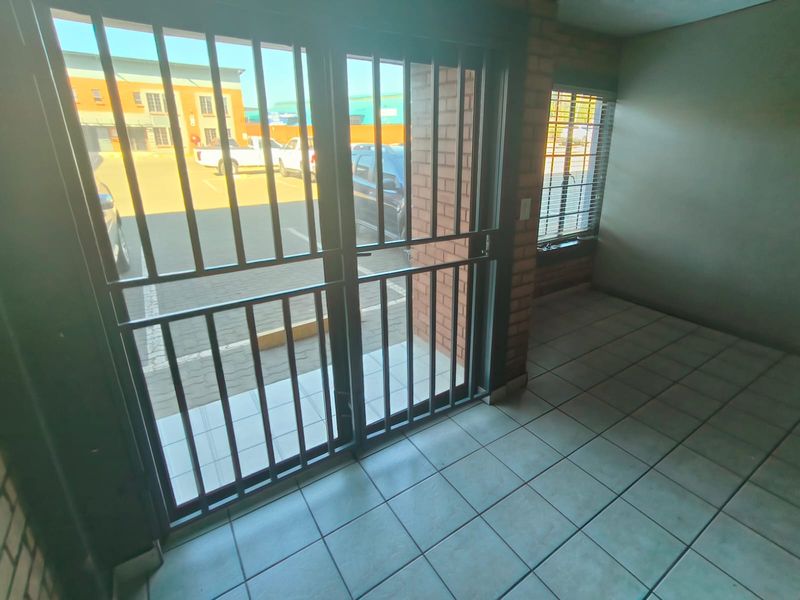 An empty industrial entry area featuring tiled flooring, exposed brick walls, and a secure metal gate leading to the exterior parking area.