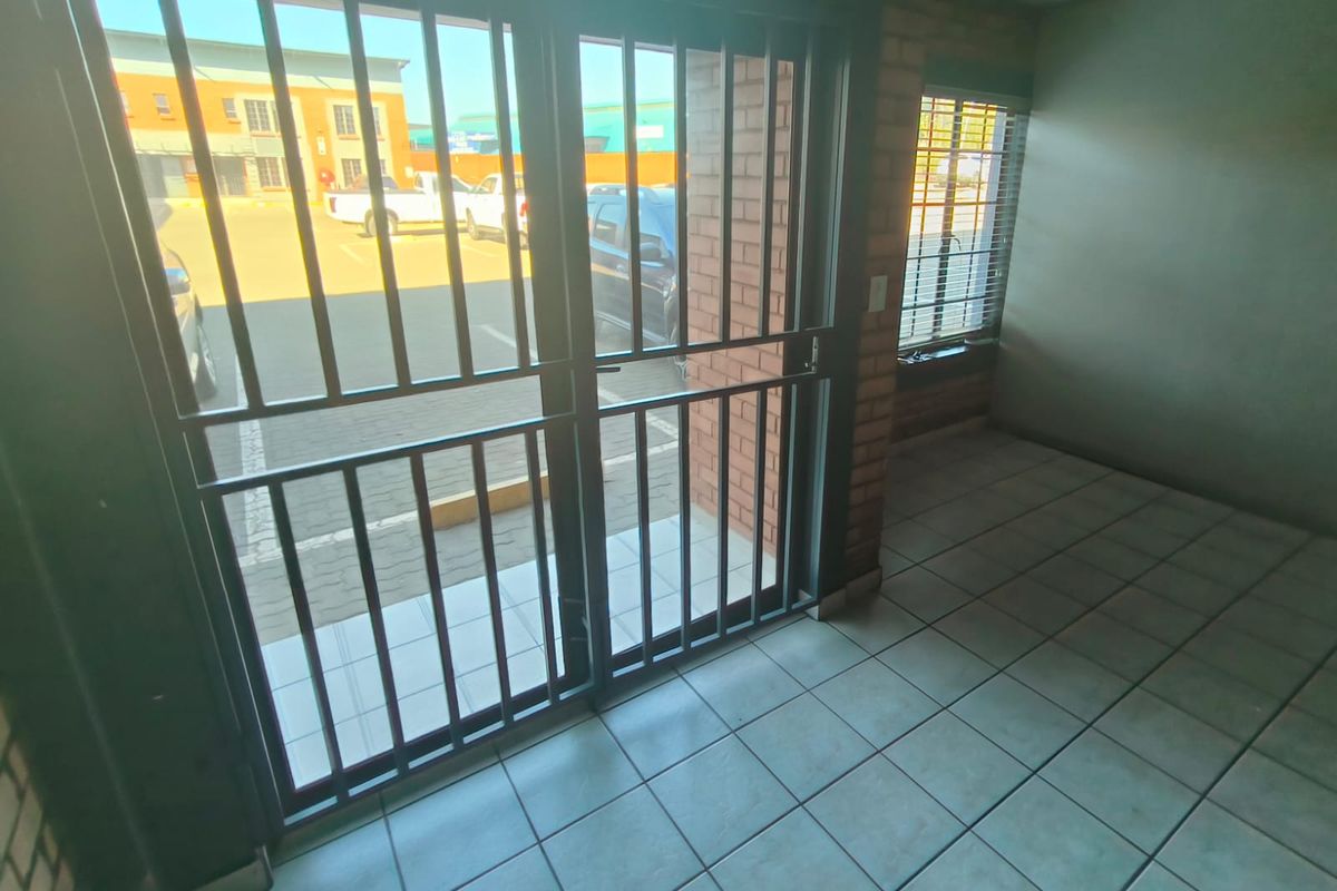 An empty industrial entry area featuring tiled flooring, exposed brick walls, and a secure metal gate leading to the exterior parking area.
