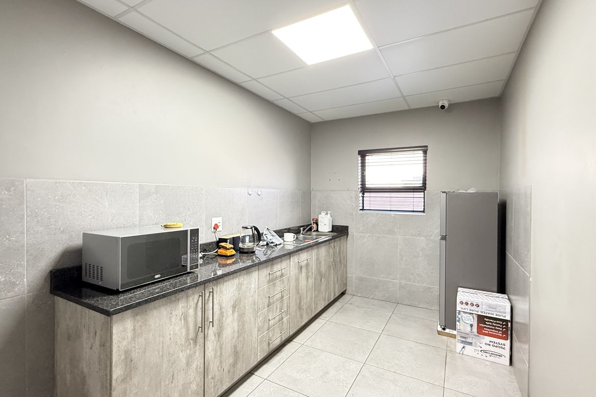 A functional industrial kitchen space featuring granite countertops, modern laminate cabinetry, tiled splashbacks, and durable floor tiles with efficient recessed lighting.