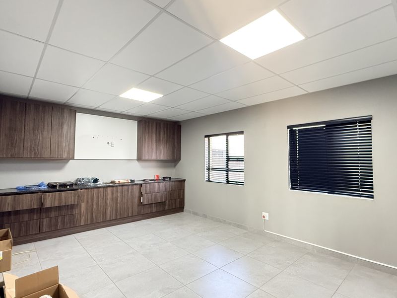Modern office space featuring a suspended ceiling with LED lighting, tiled flooring, and extensive built-in cabinetry with a dark wood finish.